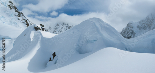 Alpine landscape of snow, mountains, hanging glaciers, rock, blue sky, clouds in the Alaska Range