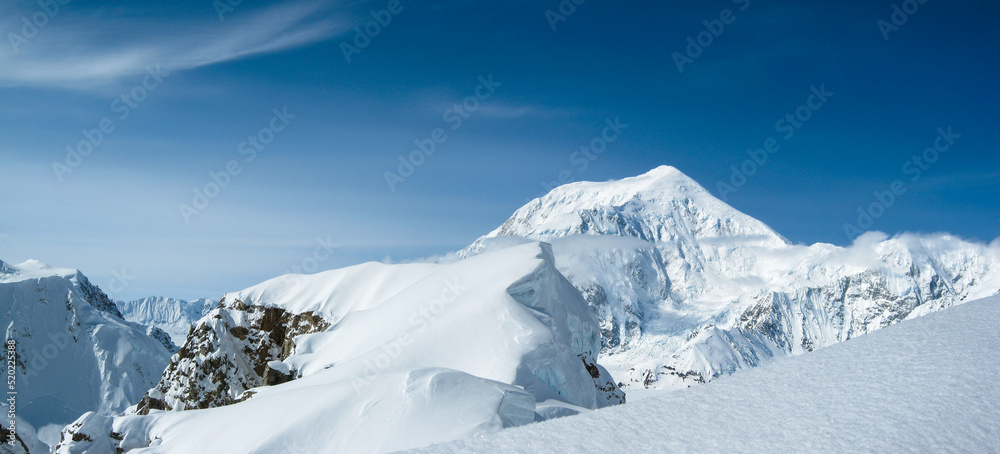 View of Mount Foraker from an adjacent peak with snow, hanging glaciers, rock, blue sky, no people