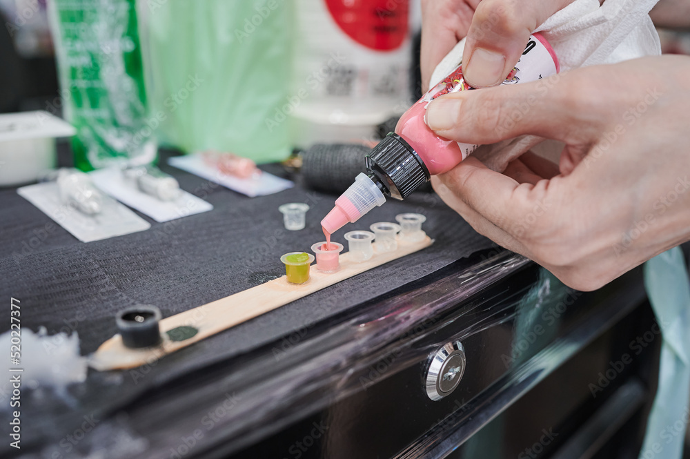 Tattoo studio scene. Pink ink refilling. Color palette on the work table of a tattoo artist to use in a design tattooed on the skin. Tattooing process.