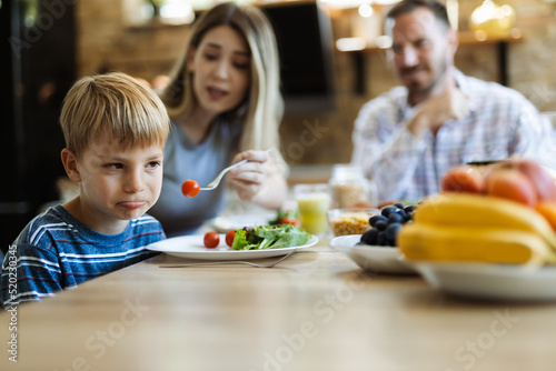 Close up of little boy refusing to eat cherry tomato offered by his mother