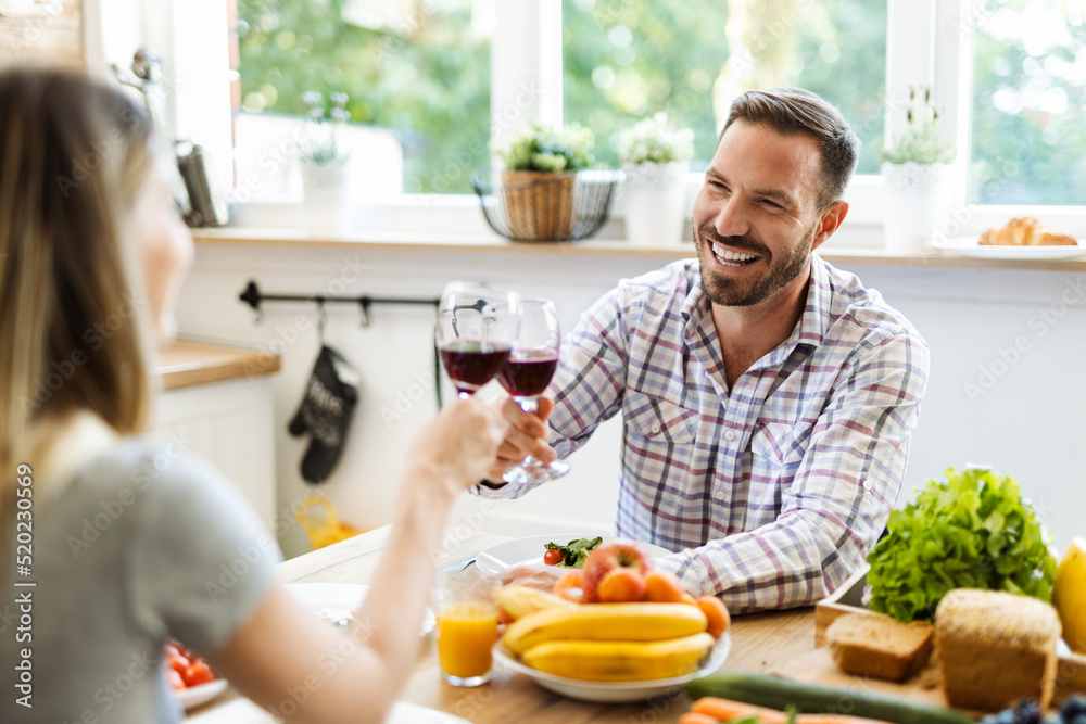 Happy young couple toasting with red wine while having lunch in dining room Happy young couple toasting with red wine while having lunch in dining room