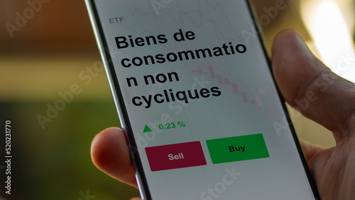 Un investisseur analyse un fonds etf biens de consommation non cycliques sur un graphique. Un téléphone affiche le cours de l'ETF Biens de consommation non cycliques