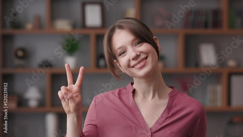 Portrait of smiling beautiful woman looking at camera. Close up portrait of Caucasian young woman gesturing V sign. Victory and peace gesture. Human face.
