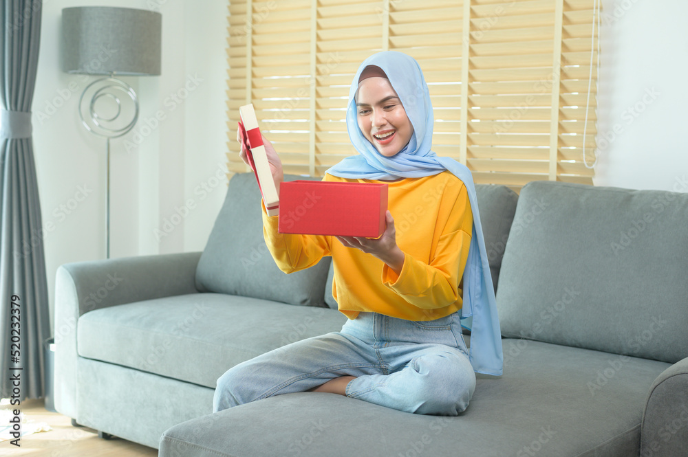Young surprised muslim woman opening a gift box in living room. Young surprised muslim woman opening a gift box in living room.
