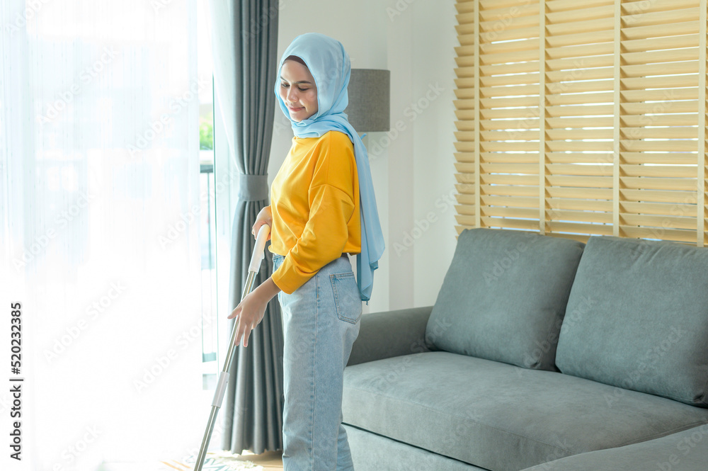 Young happy muslim woman mopping and vacuum the floor in living room.