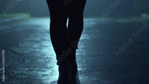 Legs of a man in backlight walking down the street at night.