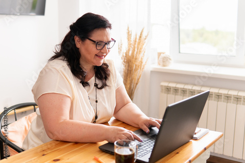 A woman is sitting in a room at a table with a laptop.