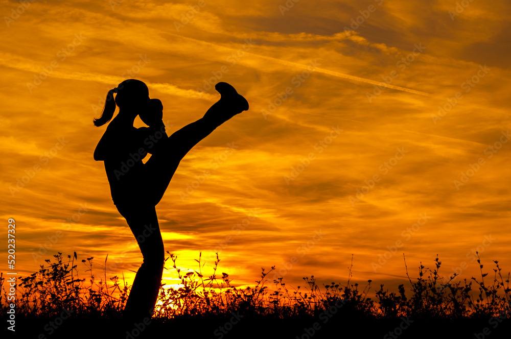 Silhouette of young woman kickboxing and exercising in the nature on a sunny summer day