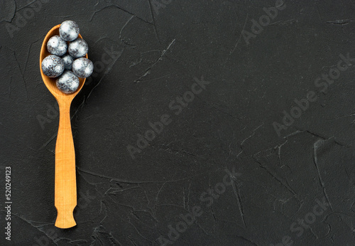 Wooden spoon with candy hazelnuts in chocolate on a dark concrete background copy space