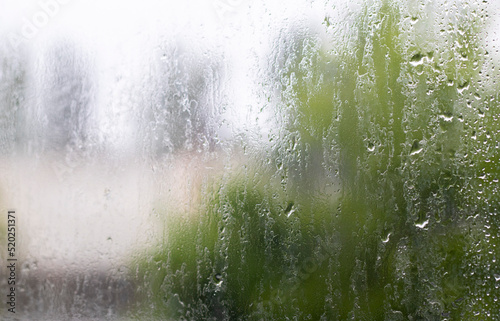 Heavy rain. Raindrops on the window glass on a summer day. Selective focus, shallow depth of field. Drops of water fall on a wet window. Glass full of drops during a downpour.