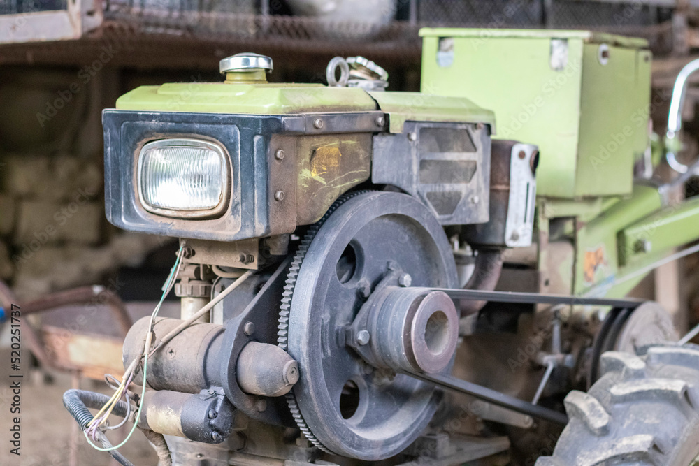 Typical heavy diesel walking tractor with trailer. Agricultural transport equipment of the countryside. Portable agricultural equipment, walking minitractor. The start system is mechanical and manual. Typical heavy diesel walking tractor with trailer. Agricultural transport equipment of the countryside. Portable agricultural equipment, walking minitractor. The start system is mechanical and manual.