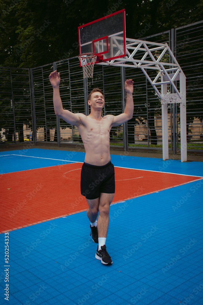 Tall athlete having fun exercising on basketball playground. Shirtless young man