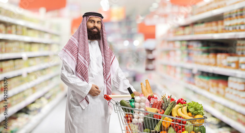 Canvas-taulu Saudi arab man with a shopping cart full of food products in a supermarket
