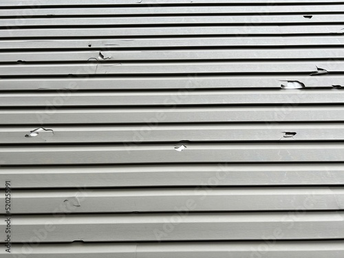 Holes in the exterior siding of the home from hail storm damage. The broken vinyl siding on a house due to hail.
