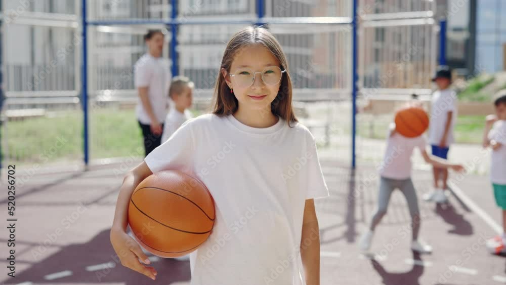 Elementary school girl standing at basketball court holding a bounce outside. Asian girl in glasses has a sport training with coach. Sport concept. Elementary school girl standing at basketball court holding a bounce outside. Asian girl in glasses has a sport training with coach. Sport concept.