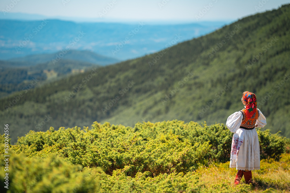 Fototapeta premium Traditional Romanian woman on top of mountain looking at green valley