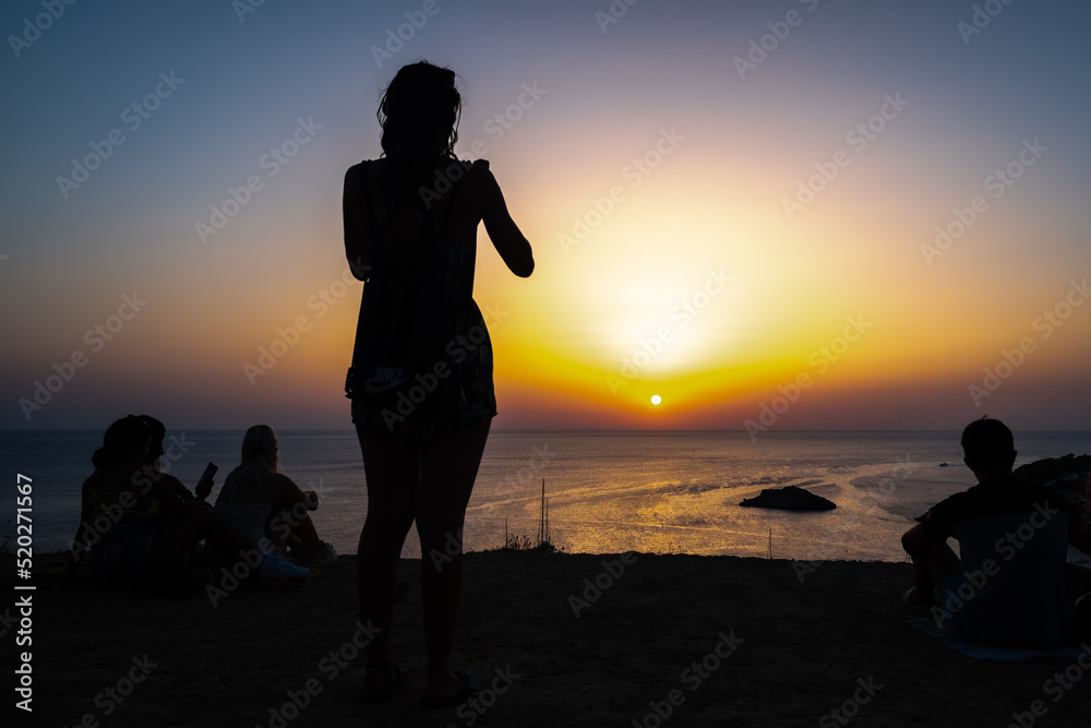 Woman enjoys the sunset on the shore of a paradisiacal beach during summer vacations.