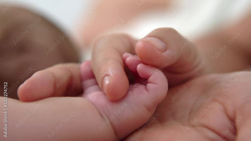 Close up baby hand holding finger mom in a room with a lot of sunlight. The newborn sleeping on the mother's bed. Health care, love and relationship concept. Close up baby hand holding finger mom in a room with a lot of sunlight. The newborn sleeping on the mother's bed. Health care, love and relationship concept.