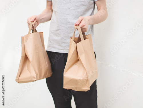 The hands of a caucasian young man hold out two paper craft bags