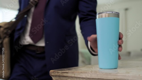 Man in blue suit picks up light blue drink when leaving for work