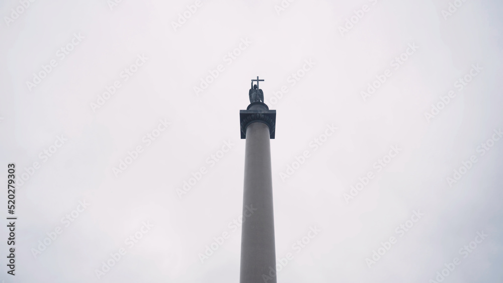 Alexandrian pillar in Saint Petersburg. Action. Bottom view of architectural monument in form of pillar with angel holding cross on top. Alexander column on background cloudy sky