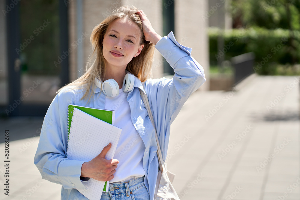 Fototapeta premium Pretty smiling girl university student holding notebooks looking at camera posing for outdoor portrait. College study programs, academic education ads, admission and scholarship.