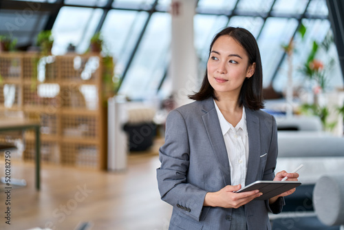 Young Asian business woman entrepreneur standing in office holding digital tablet. Businesswoman leader, professional company manager using smart corporate management technology looking at copy space.