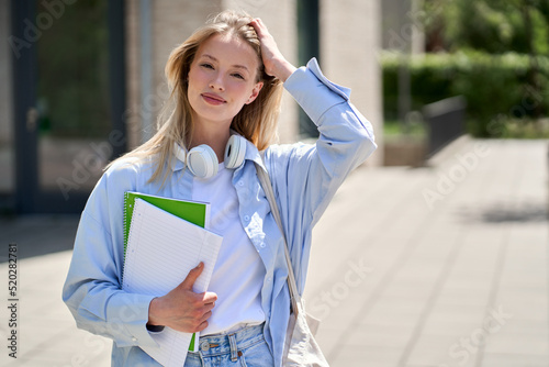 Fotografie Pretty smiling girl university student holding notebooks looking at camera posing for outdoor portrait