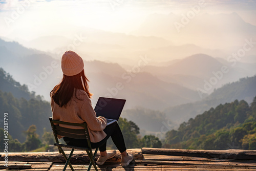 Young woman freelancer traveler working online using laptop and enjoying the beautiful nature landscape with mountain view at sunrise photo