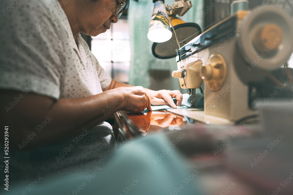 Naklejka premium Retriement tailor southeast asian elderly crafting a cloth by sewing machine working at home