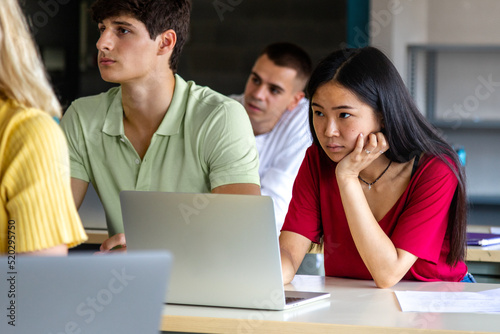 Asian female teen college student in class listening to lecture using laptop to take notes.