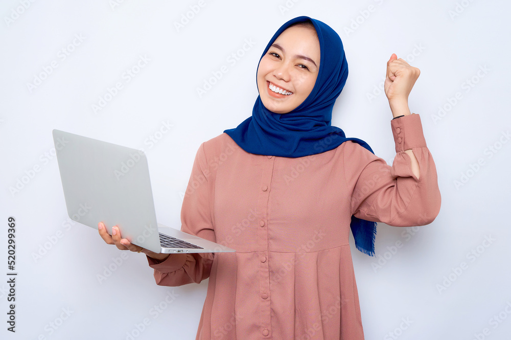 Cheerful young Asian muslim woman in pink shirt holding laptop,celebrating success isolated over white background. People religious lifestyle concept Cheerful young Asian muslim woman in pink shirt holding laptop,celebrating success isolated over white background. People religious lifestyle concept