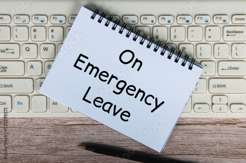 On emergency leave text on white notepad with pen and keyboard background.