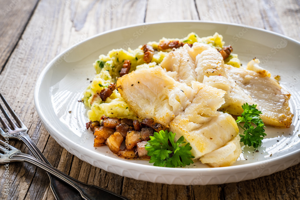 Fish dish - fried cod fillet with potato puree and bacon on wooden table
