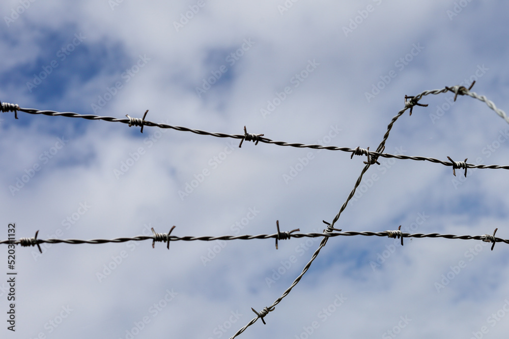 Steel fence and barbed wire detail with clouds and sky background Steel fence and barbed wire detail with clouds and sky background