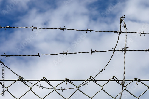 Steel fence and barbed wire detail with clouds and sky background
