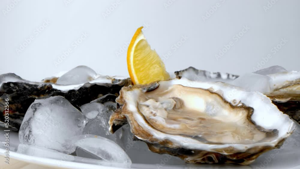 Oysters on ice with lemon closeup. Fresh Oyster on half shell on big plate in restaurant. Served table. 4K UHD video slow motion Oysters on ice with lemon closeup. Fresh Oyster on half shell on big plate in restaurant. Served table. 4K UHD video slow motion