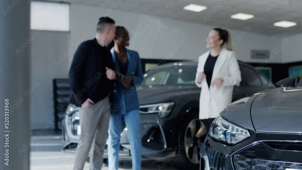 Portrait of a smiling african lady and her european man inspecting the interior of a new car in a modern dealership. An attractive salesperson talks about an electric car and enjoys the beautiful car Portrait of a smiling african lady and her european man inspecting the interior of a new car in a modern dealership. An attractive salesperson talks about an electric car and enjoys the beautiful car