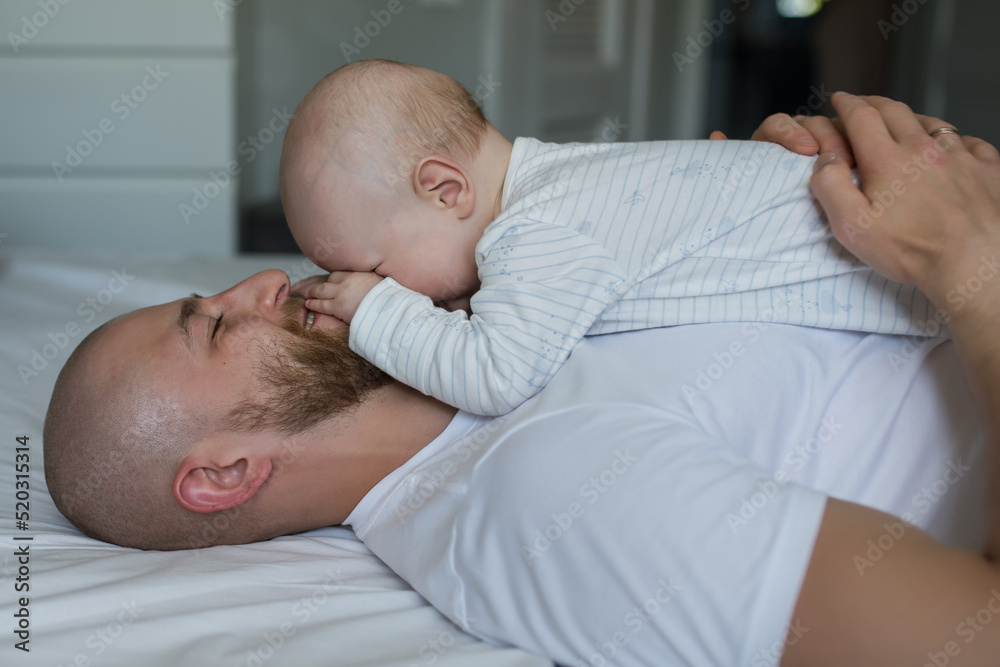 happy young father lies on the bed and holds his newborn son on his stomach, dad and son are resting, lying on the bed, the concept of care and love, father's day happy young father lies on the bed and holds his newborn son on his stomach, dad and son are resting, lying on the bed, the concept of care and love, father's day