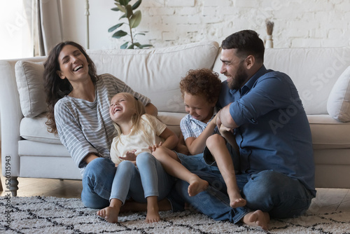 Fotografija Happy parents cuddling, tickling little children on floor, laughing, having fun, enjoying family activity, leisure