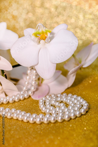 white Orchid and pearl necklace on a shiny gold background 