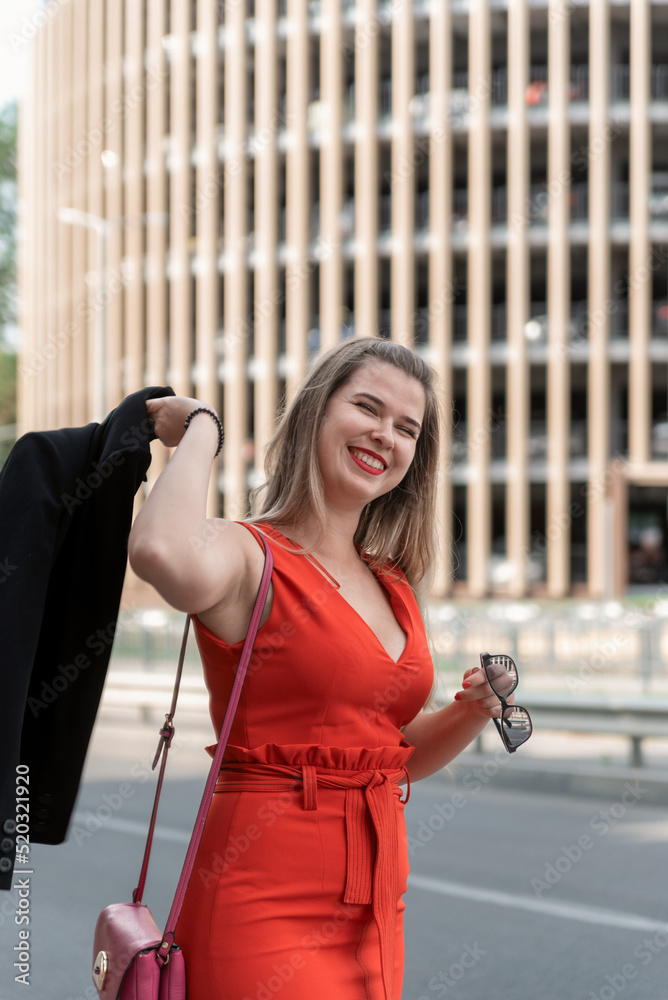 Happy successful young business woman in red dress swings jacket over her head. Smiling beautiful woman. Vertical frame.