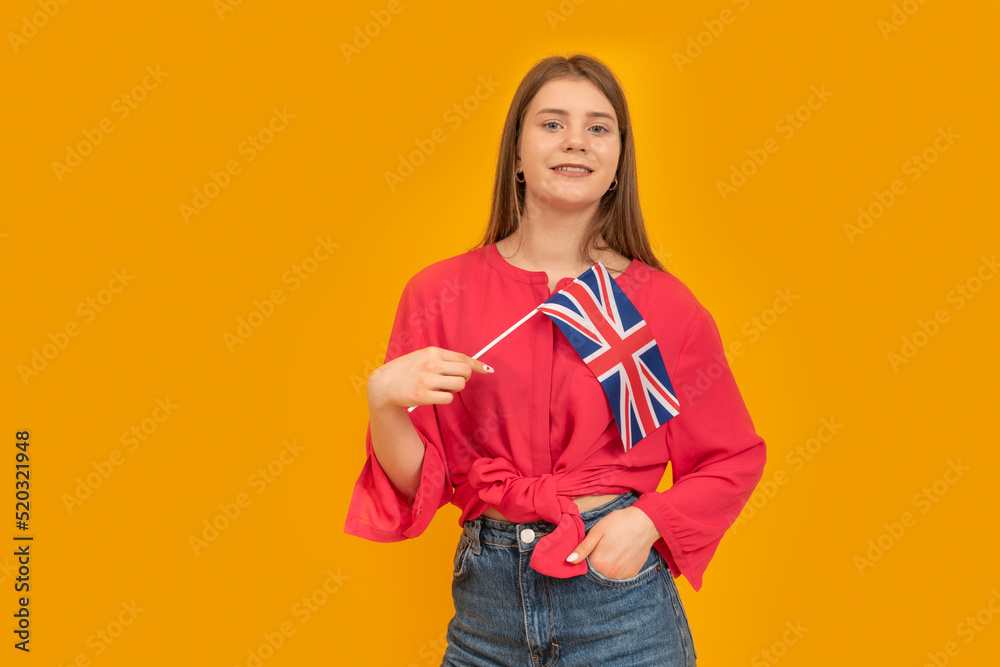 Teenage girl holds the flag of Great Britain on an orange background. Study English. Immigration to the UK. Teenage girl holds the flag of Great Britain on an orange background. Study English. Immigration to the UK.