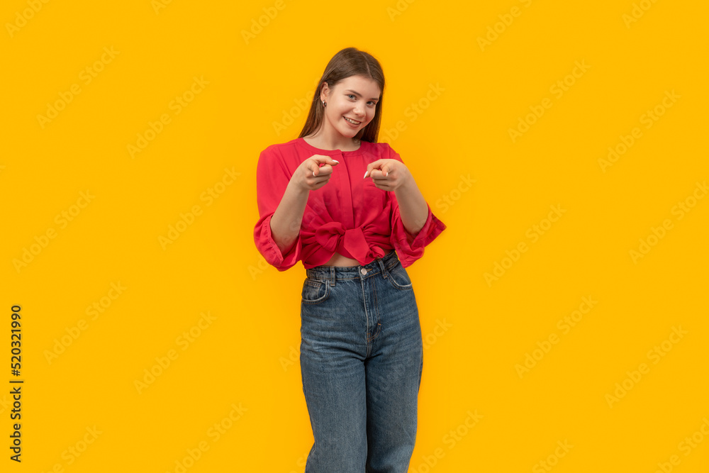 Attractive student girl in youth clothes looks into camera and points fingers at you. Portrait on yellow background. Mock up copy space. Attractive student girl in youth clothes looks into camera and points fingers at you. Portrait on yellow background. Mock up copy space.