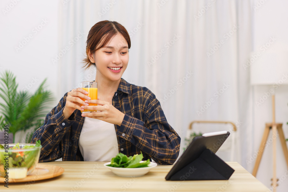 Lifestyle in living room concept, Asian woman watching movie on tablet and drinking orange juice