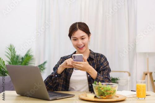 Lifestyle in living room concept  Young Asian woman using smartphone and eating vegetable salad