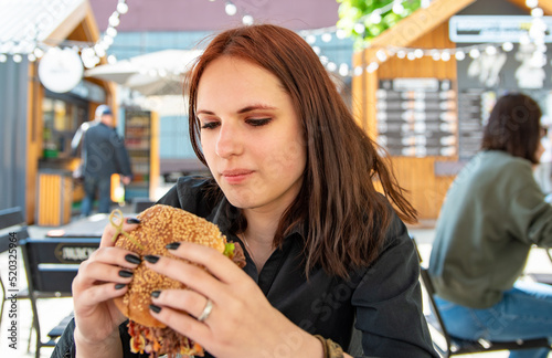 Woman eating street food burger outdoors. Traditional barbecue pulled beef burger with vegetables in woman hand