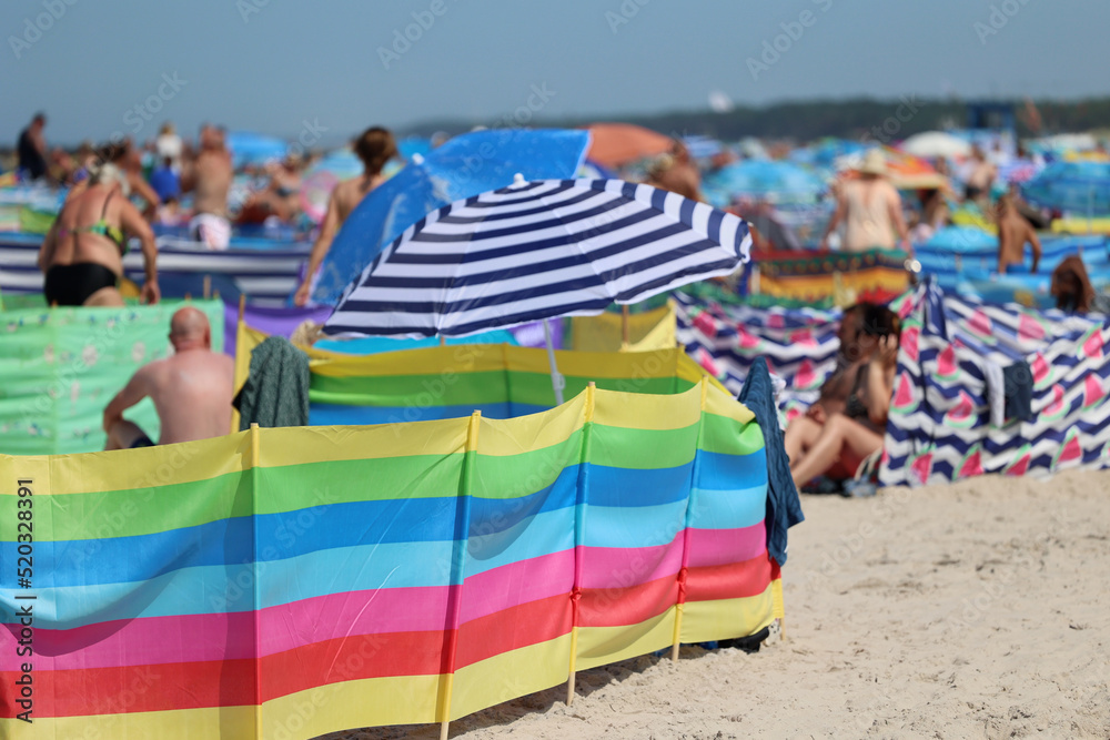 Parasol słoneczny na plaży nadmorskiej w wakacje razem z parawanem na wiatr.
 - obrazy, fototapety, plakaty 