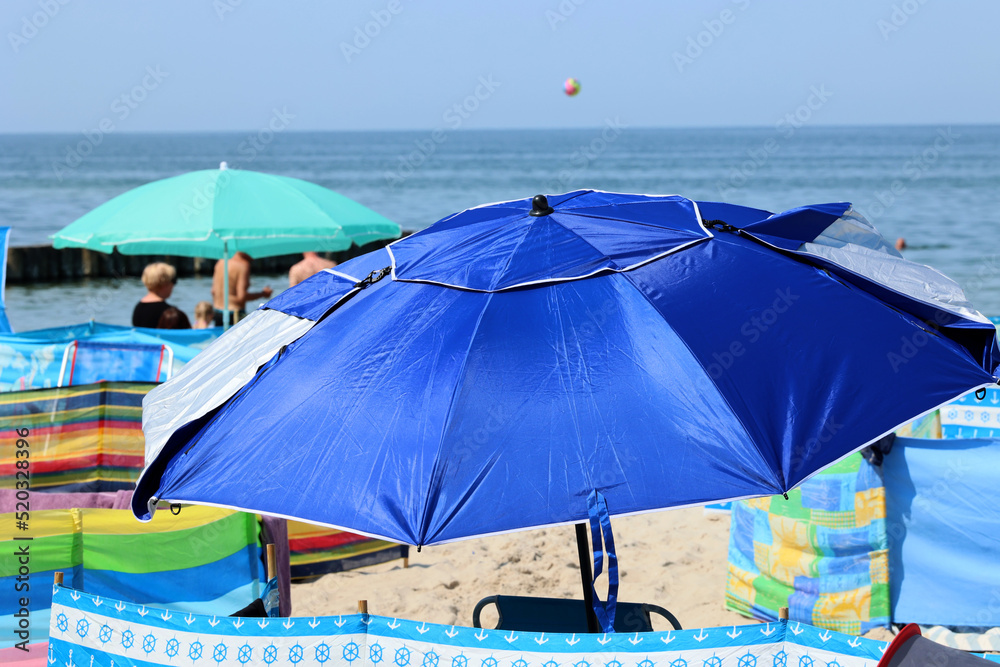 Parasol słoneczny na plaży nadmorskiej w wakacje razem z parawanem na wiatr.
 - obrazy, fototapety, plakaty 