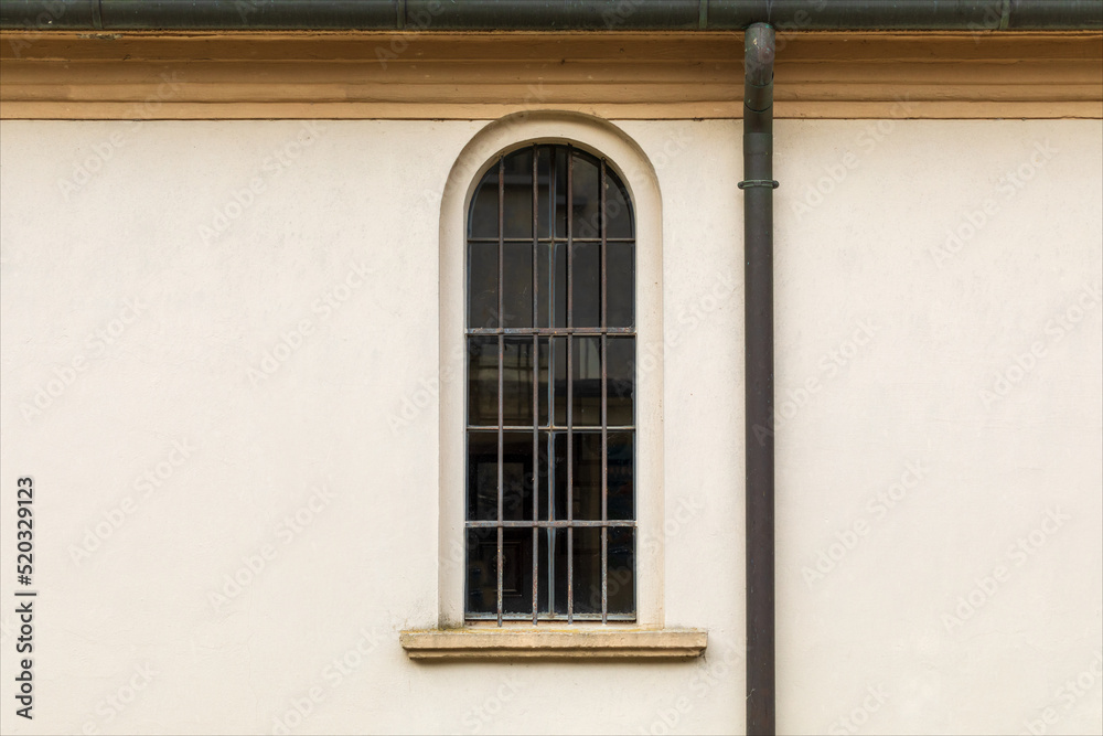 Vecchia finestra a vetro stretta ed a arco su facciata di edificio religioso con visibile la grondaia esterna.